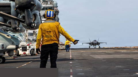 A U.S. Navy sailor is guiding an F-35B fighter on the flight deck of the amphibious assault ship USS Boxer (LHD-4) (L…